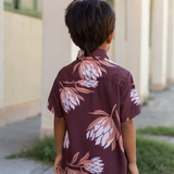 little boy wearing brown mini button up aloha shirt with protea print