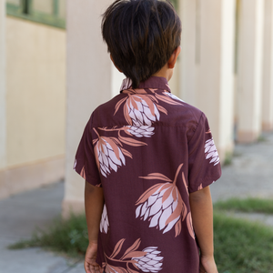 little boy wearing brown mini button up aloha shirt with protea print