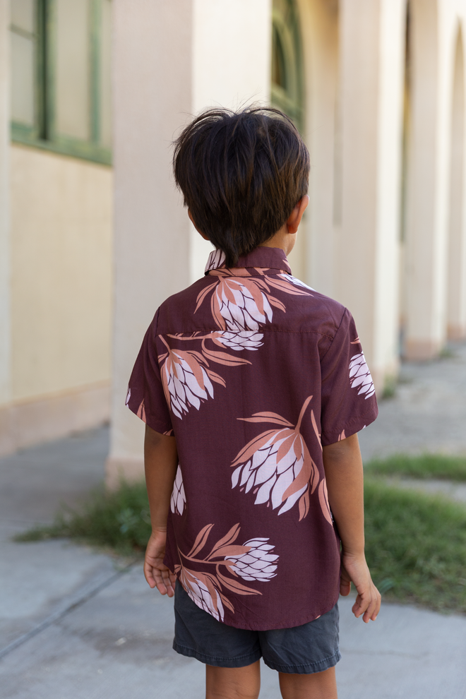 little boy wearing brown mini button up aloha shirt with protea print