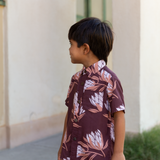 little boy wearing brown mini button up aloha shirt with protea print