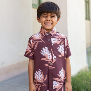 little boy wearing brown mini button up aloha shirt with protea print