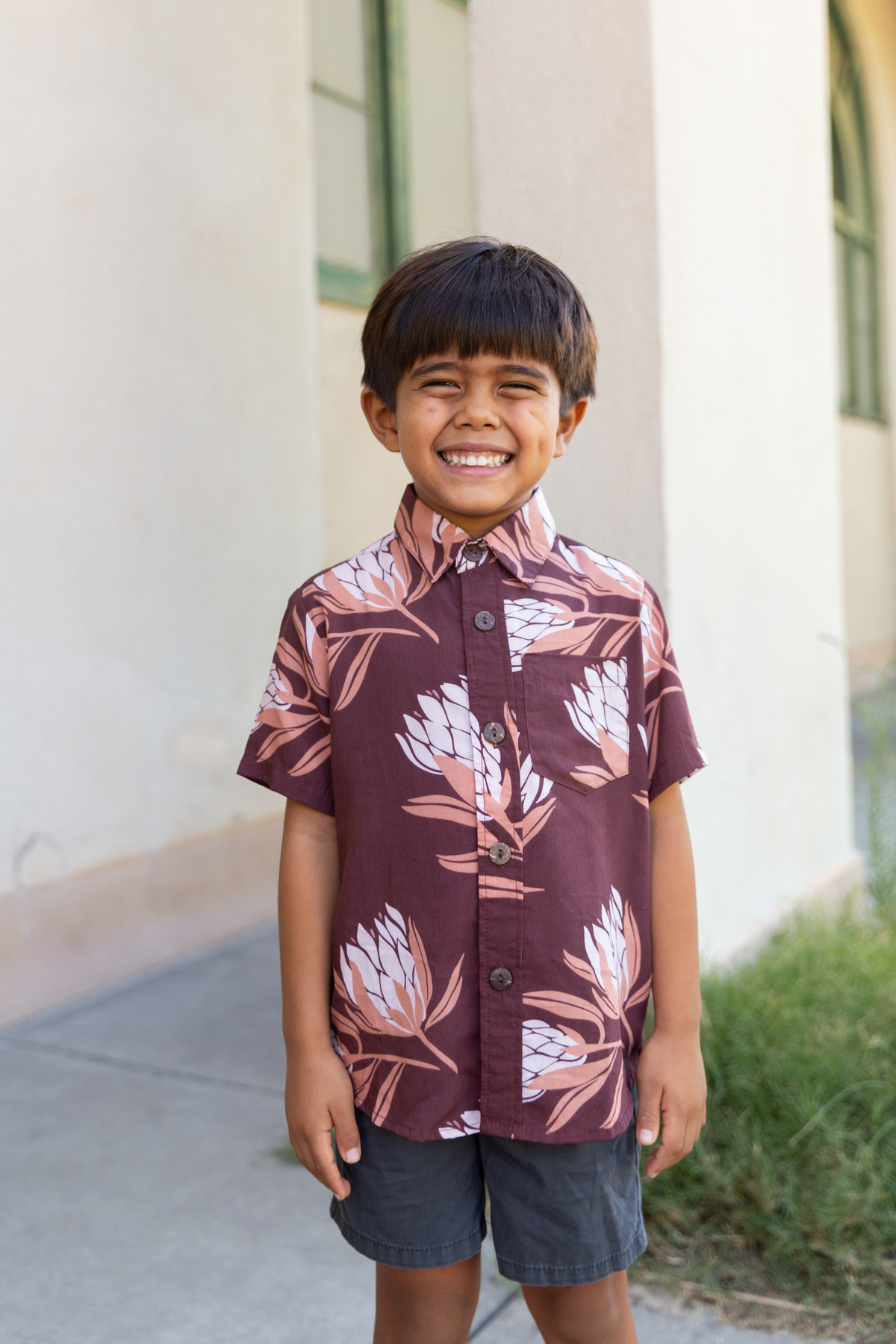little boy wearing brown mini button up aloha shirt with protea print