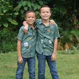 little boy wearing lush green aloha button up shirt with pua kenikeni print