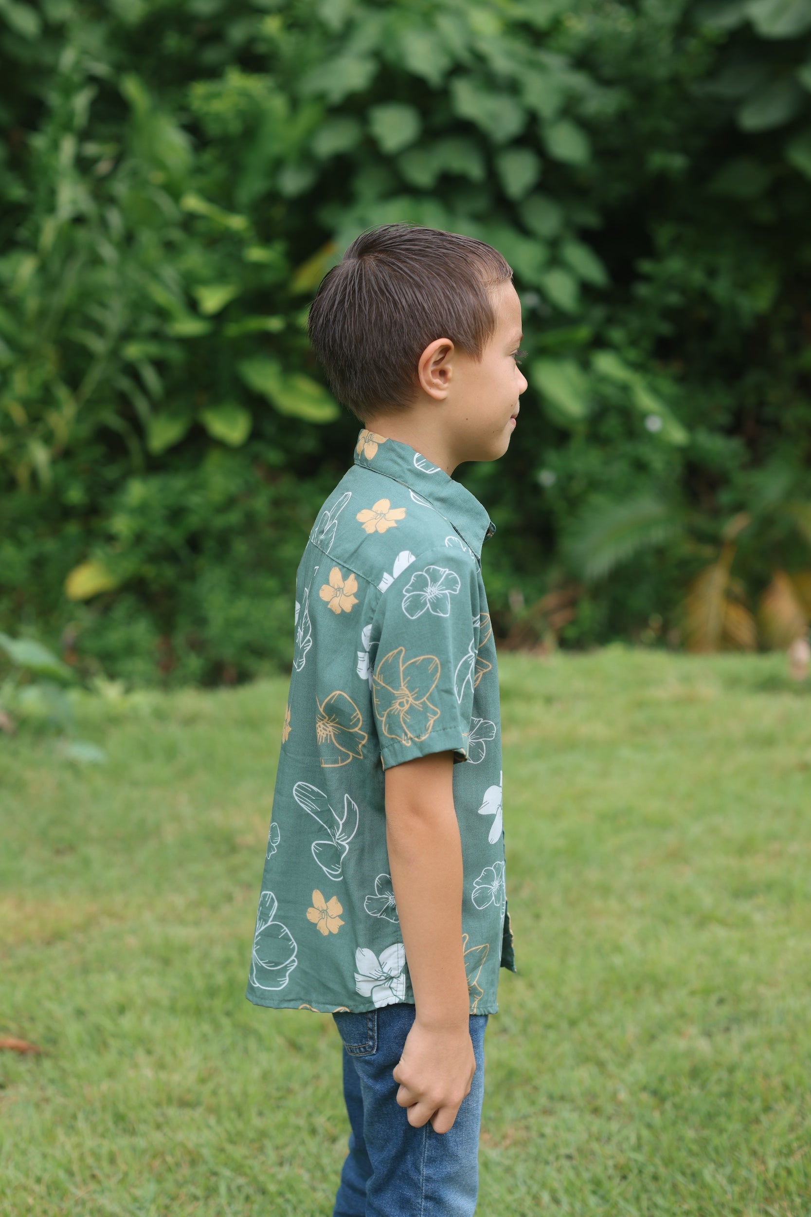 little boy wearing lush green aloha button up shirt with pua kenikeni print