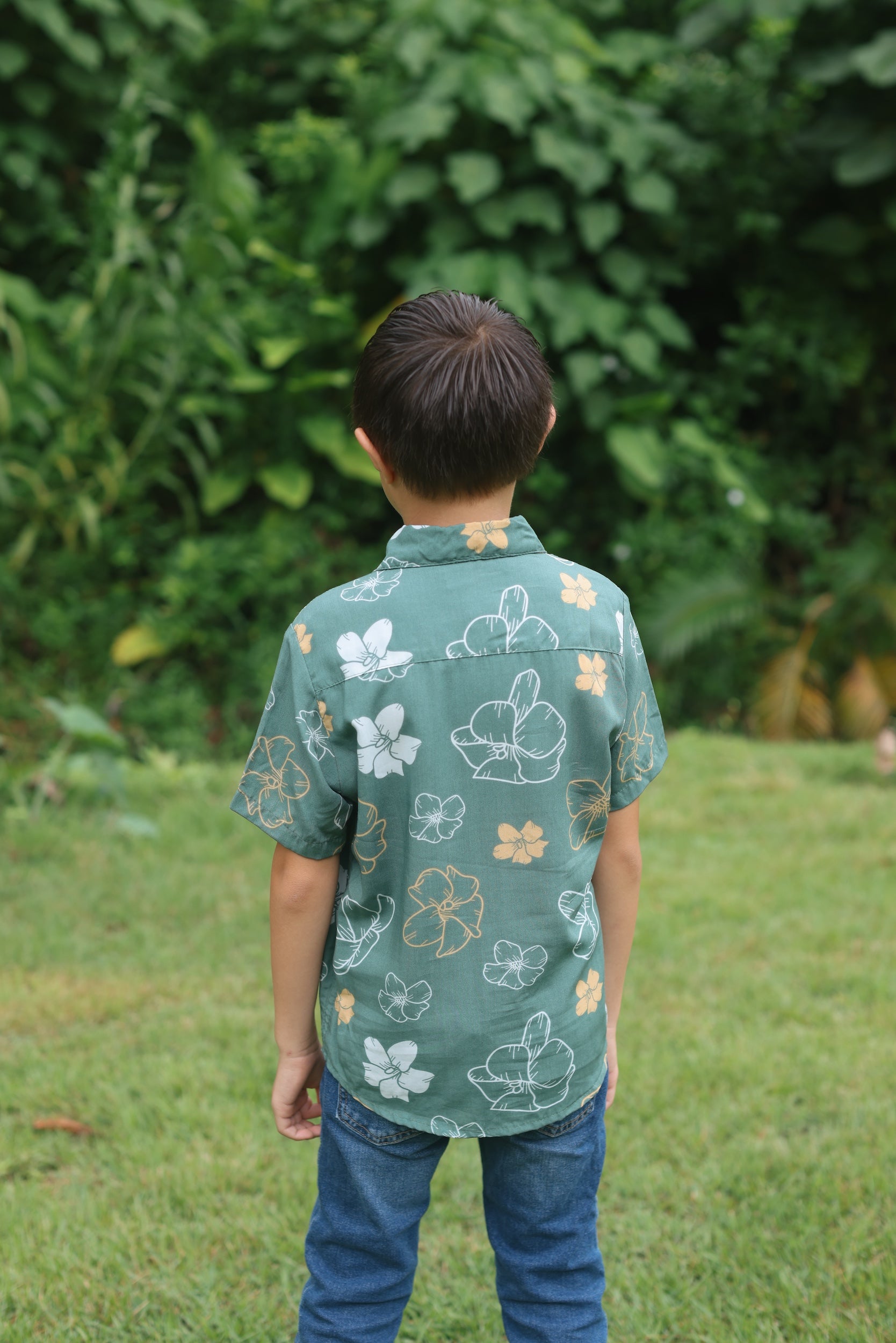 little boy wearing lush green aloha button up shirt with pua kenikeni print