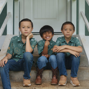 little boy wearing lush green aloha button up shirt with pua kenikeni print