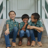 little boy wearing lush green aloha button up shirt with pua kenikeni print