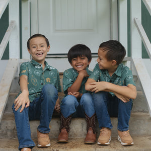 little boy wearing lush green aloha button up shirt with pua kenikeni print