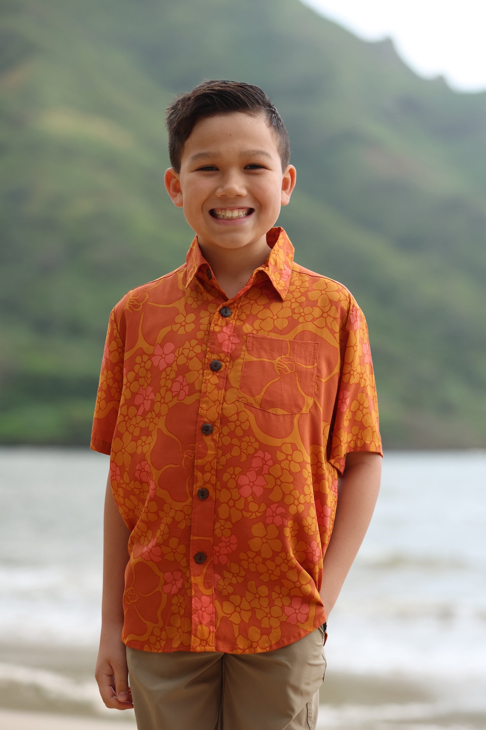little boy wearing orange aloha button up shirt with puakenikeni print