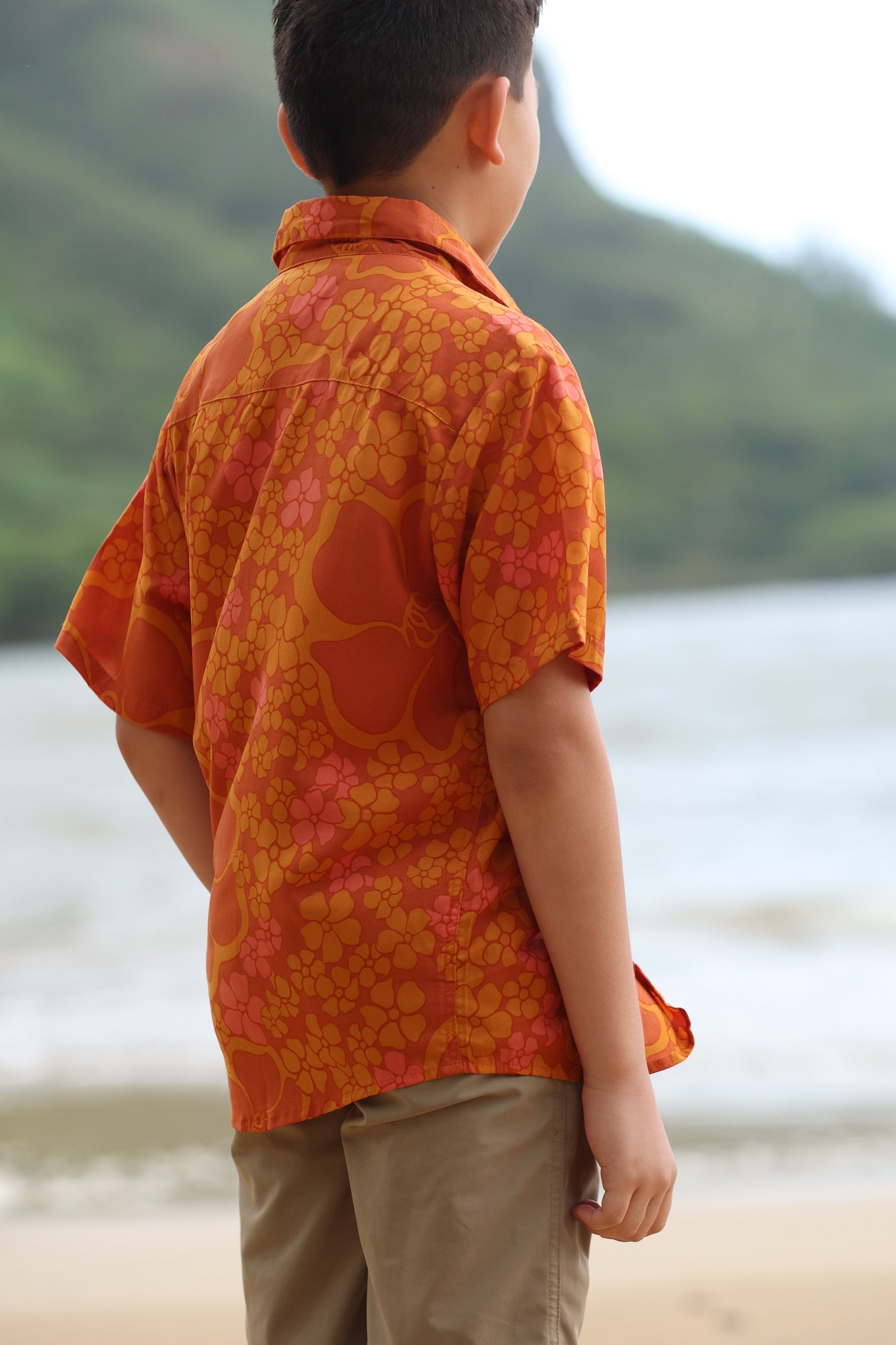little boy wearing orange aloha button up shirt with puakenikeni print
