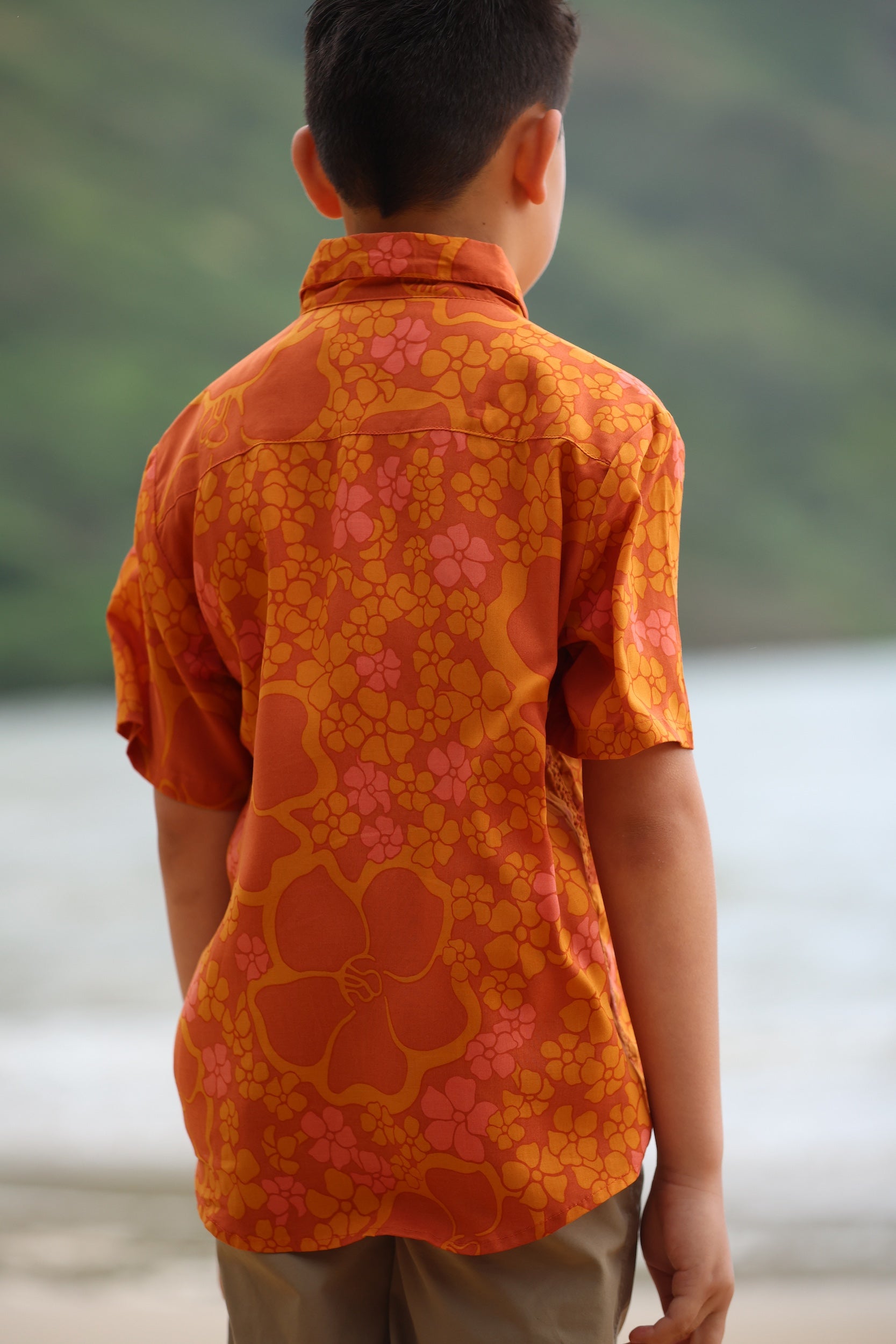 little boy wearing orange aloha button up shirt with puakenikeni print