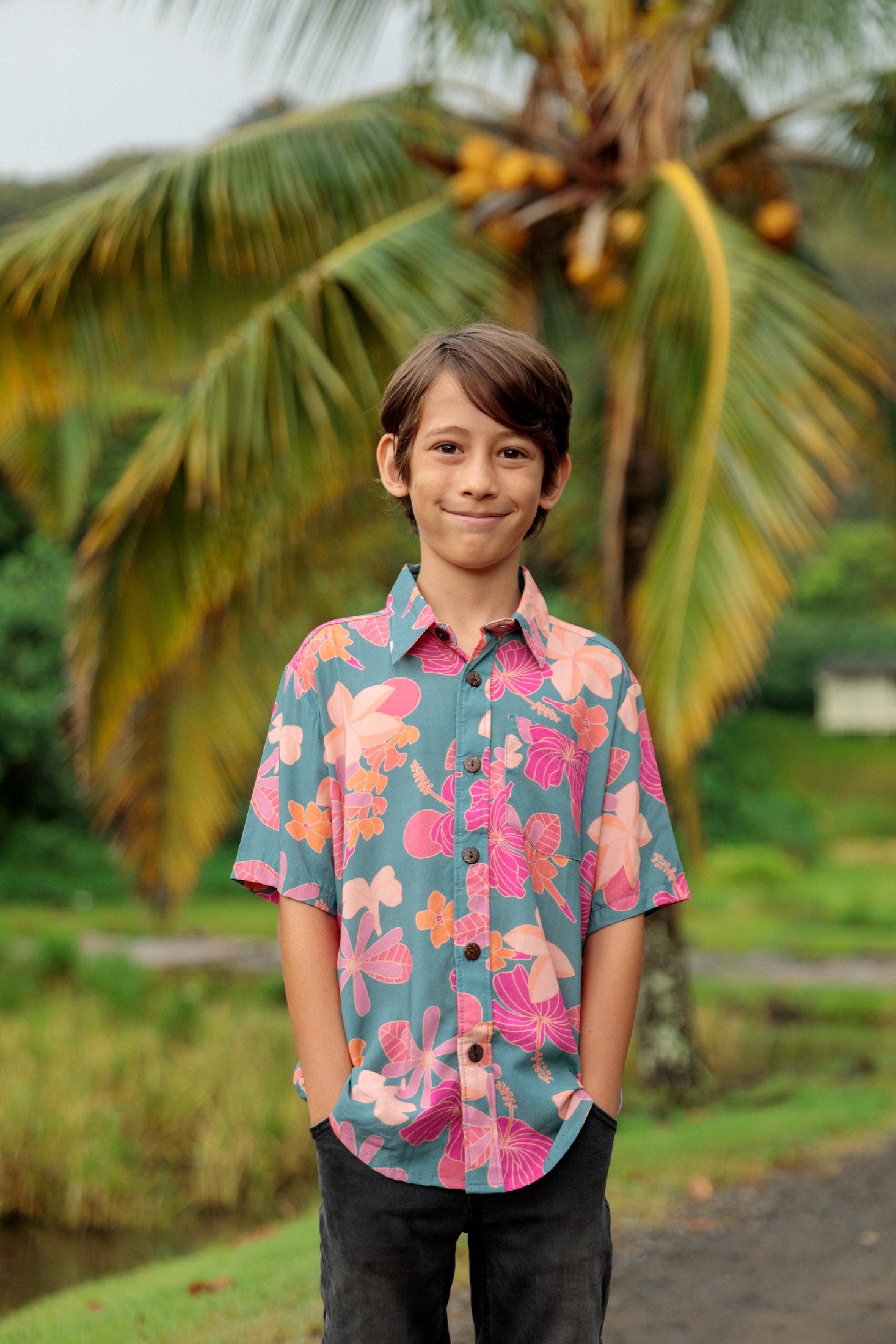little boy wearing a teal button up aloha shirt with floral pattern