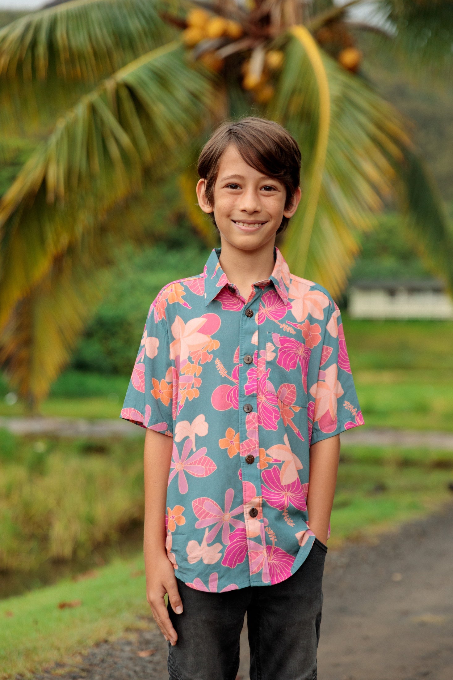 little boy wearing a teal button up aloha shirt with floral pattern