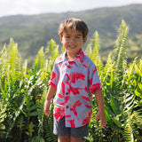 little boy with brown hair wearing a button up aloha shirt with periwinkle background and bright red hibiscus print.