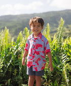 little boy with brown hair wearing a button up aloha shirt with periwinkle background and bright red hibiscus print.