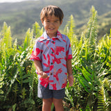 little boy with brown hair wearing a button up aloha shirt with periwinkle background and bright red hibiscus print.