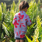 little boy with brown hair wearing a button up aloha shirt with periwinkle background and bright red hibiscus print.