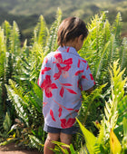 little boy with brown hair wearing a button up aloha shirt with periwinkle background and bright red hibiscus print.