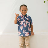 little boy wearing button up aloha shirt in navy and pink hibiscus print.