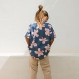 little boy wearing button up aloha shirt in navy and pink hibiscus print.
