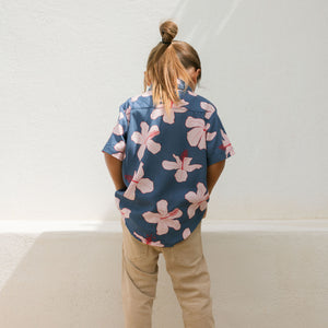 little boy wearing button up aloha shirt in navy and pink hibiscus print.