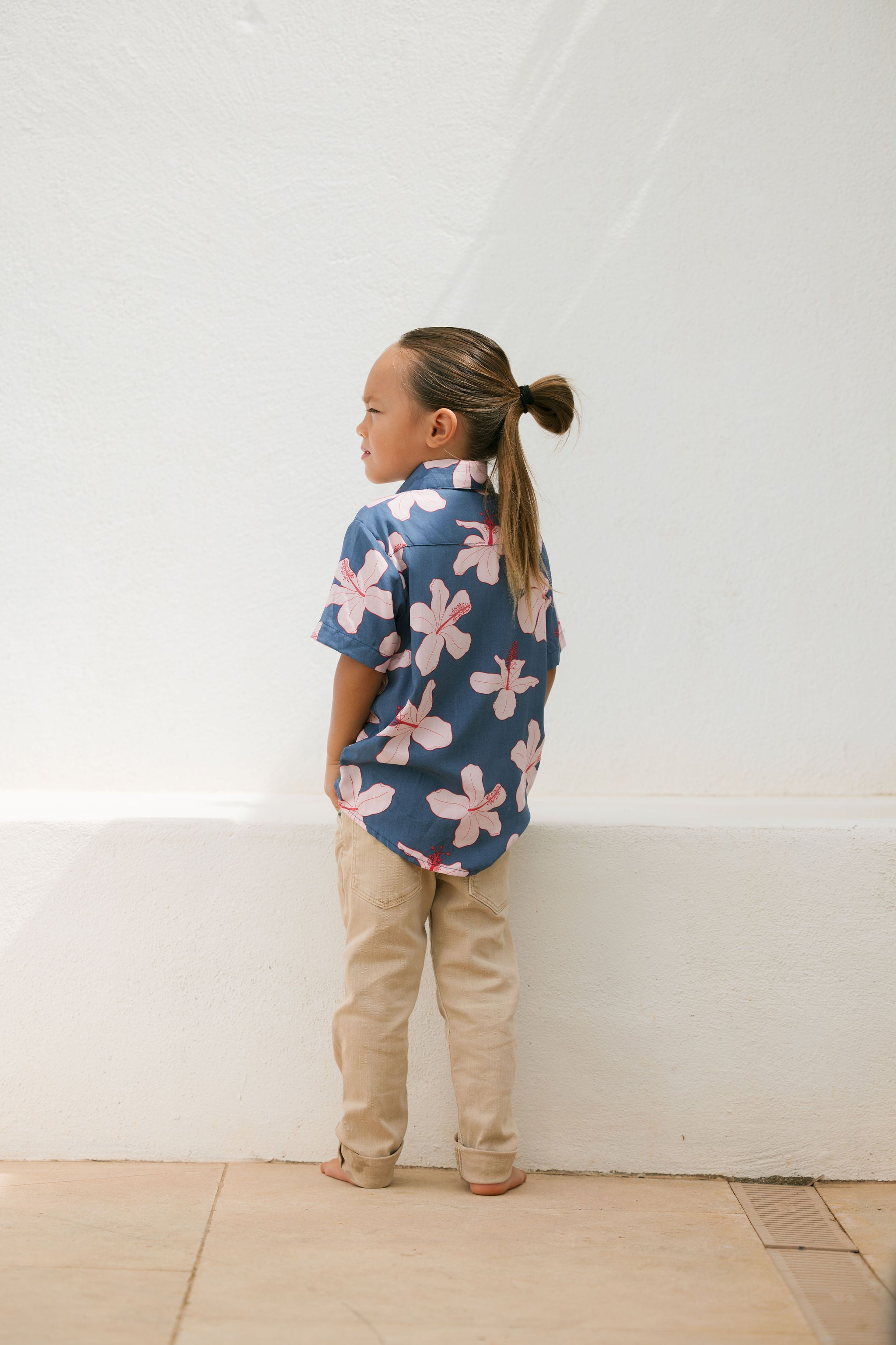 little boy wearing button up aloha shirt in navy and pink hibiscus print.