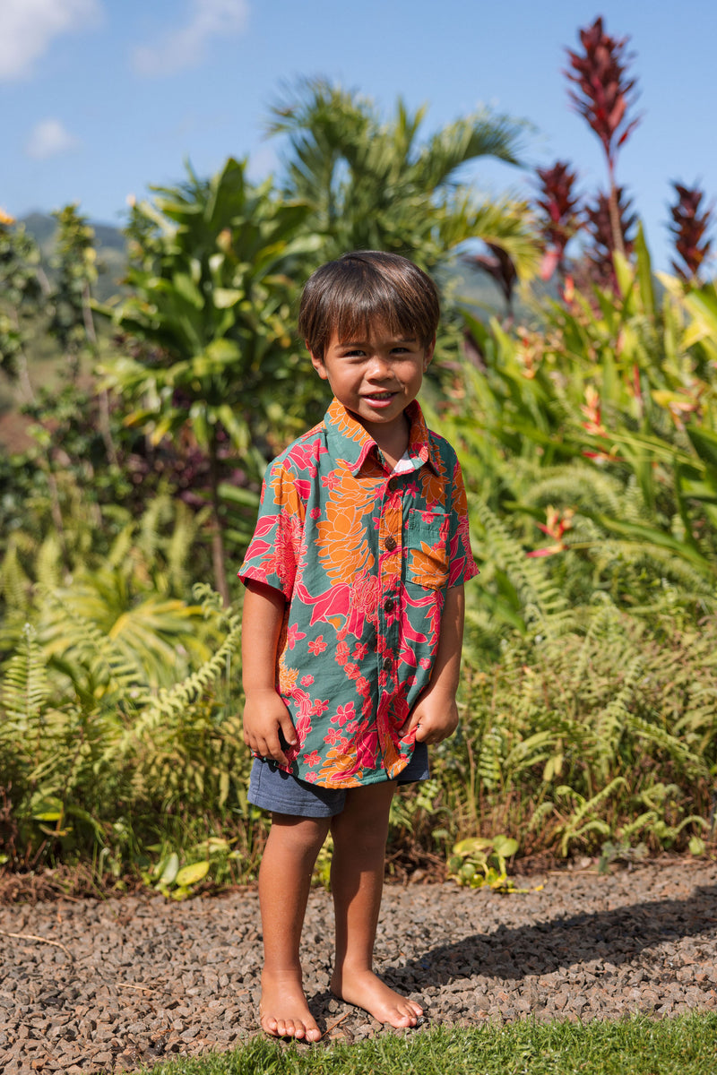 boy with brown hair wearing a colorful button up aloha shirt with tropical lei print