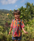 boy with brown hair wearing a colorful button up aloha shirt with tropical lei print