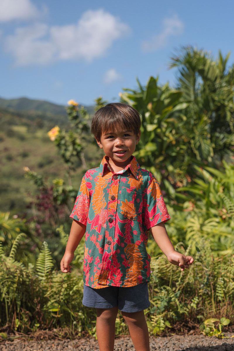 boy with brown hair wearing a colorful button up aloha shirt with tropical lei print
