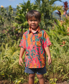 boy with brown hair wearing a colorful button up aloha shirt with tropical lei print