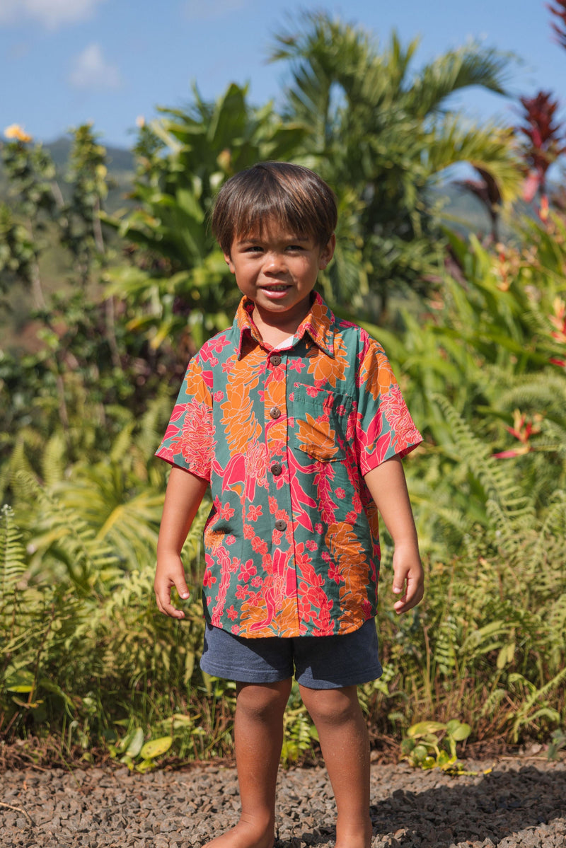 boy with brown hair wearing a colorful button up aloha shirt with tropical lei print