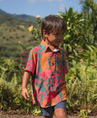 boy with brown hair wearing a colorful button up aloha shirt with tropical lei print