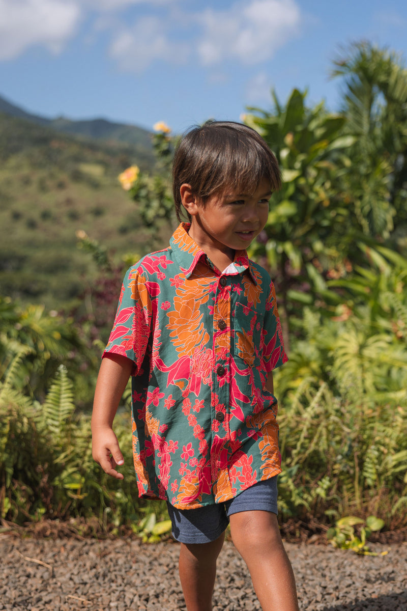 boy with brown hair wearing a colorful button up aloha shirt with tropical lei print