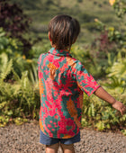 boy with brown hair wearing a colorful button up aloha shirt with tropical lei print