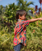 boy with brown hair wearing a colorful button up aloha shirt with tropical lei print