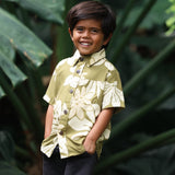 little boy wearing mini aloha button up shirt in green print and naupaka pattern