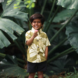little boy wearing mini aloha button up shirt in green print and naupaka pattern