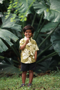 little boy wearing mini aloha button up shirt in green print and naupaka pattern