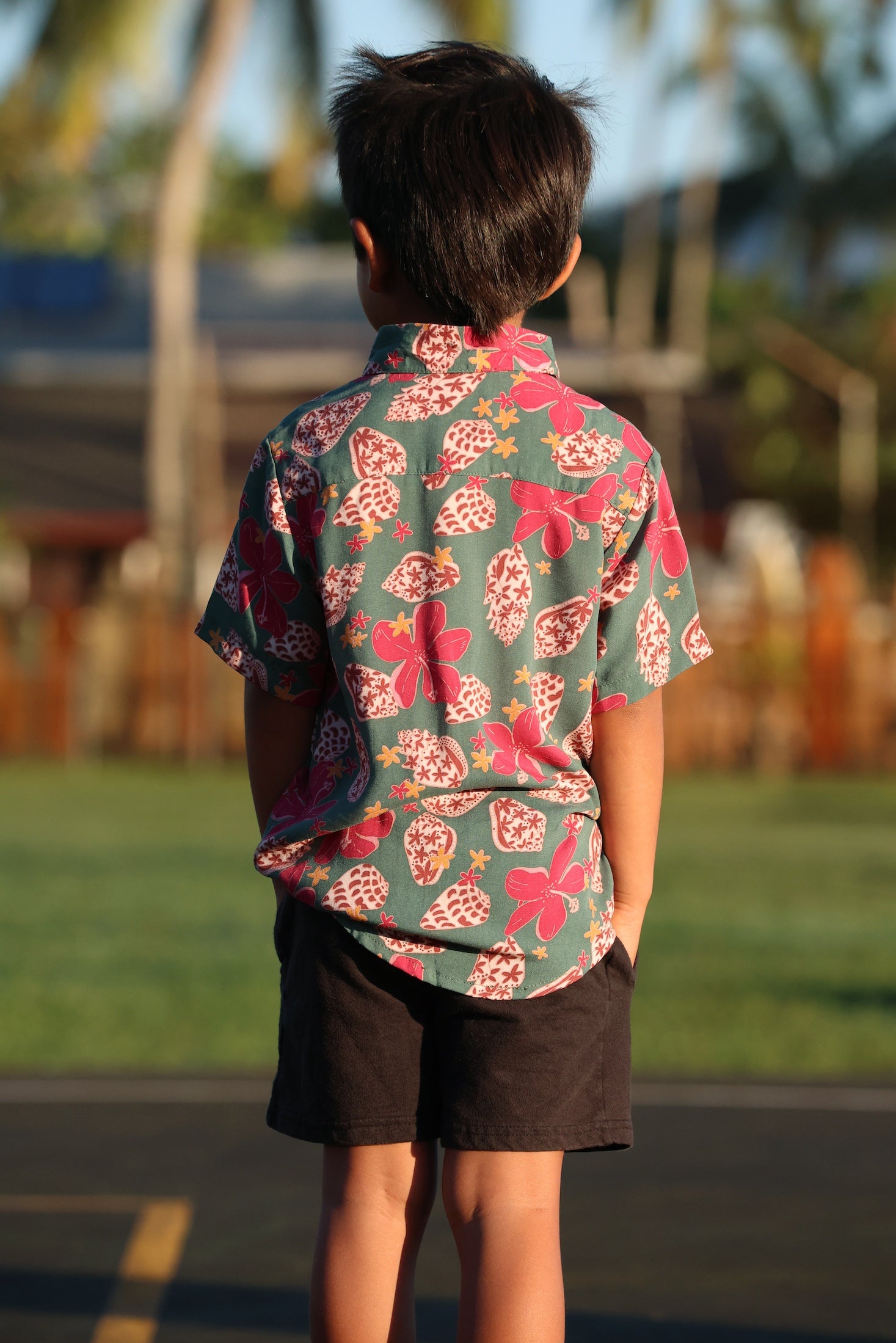 little boy wearing a teal aloha shirt with shell and pua print 