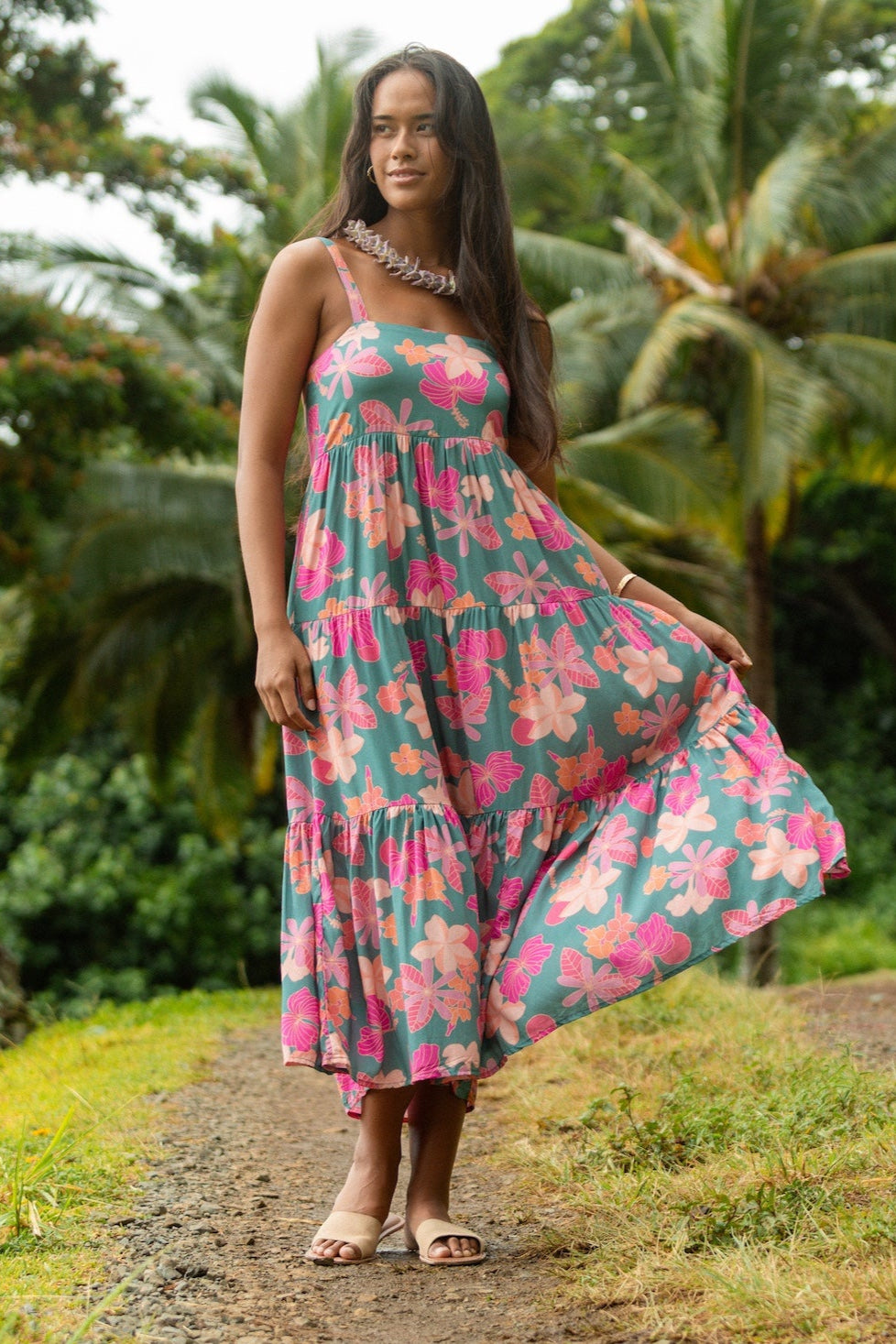 woman with brown hair wearing a teal maxi dress with orange and pink floral print