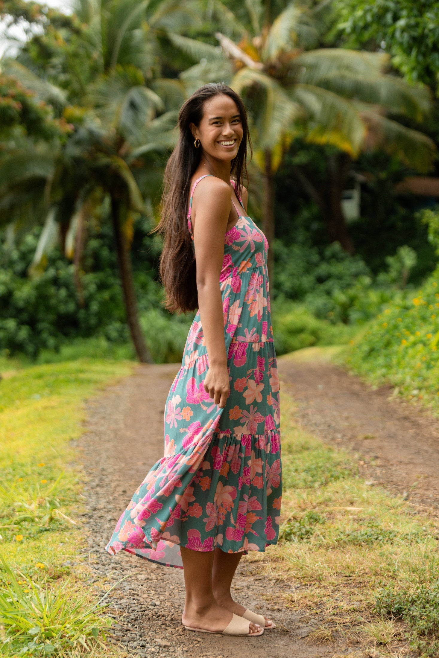 woman with brown hair wearing a teal maxi dress with orange and pink floral print