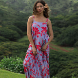 woman with brown hair wearing a flowy maxi dress with periwinkle background and bright red hibiscus print.