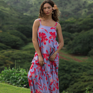 woman with brown hair wearing a flowy maxi dress with periwinkle background and bright red hibiscus print.