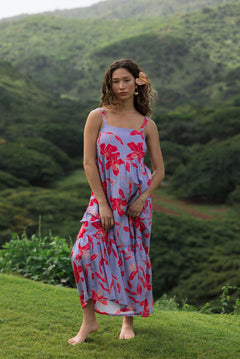 woman with brown hair wearing a flowy maxi dress with periwinkle background and bright red hibiscus print.