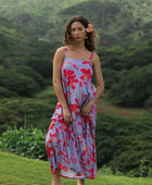 woman with brown hair wearing a flowy maxi dress with periwinkle background and bright red hibiscus print.