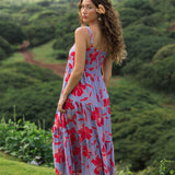 woman with brown hair wearing a flowy maxi dress with periwinkle background and bright red hibiscus print.