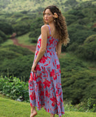 woman with brown hair wearing a flowy maxi dress with periwinkle background and bright red hibiscus print.