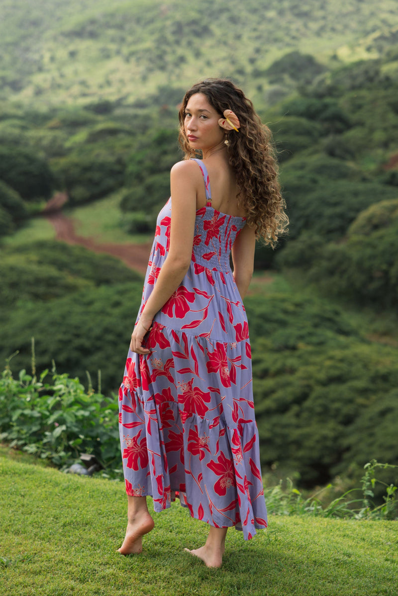 woman with brown hair wearing a flowy maxi dress with periwinkle background and bright red hibiscus print.