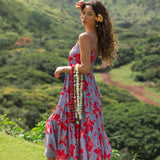 woman with brown hair wearing a flowy maxi dress with periwinkle background and bright red hibiscus print.