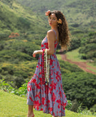 woman with brown hair wearing a flowy maxi dress with periwinkle background and bright red hibiscus print.